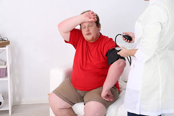 Das Bild zeigt einen übergewichtigen Mann, dem Blutdruck gemessen wird.